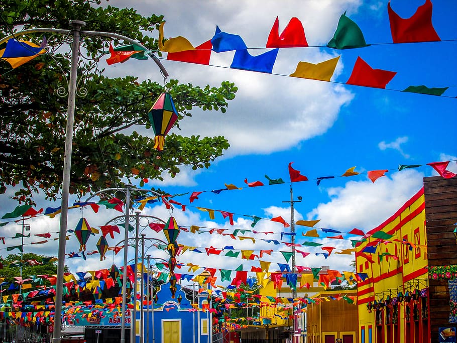 Festa junina animada, com pessoas dançando quadrilha e barracas de comidas típicas ao fundo.